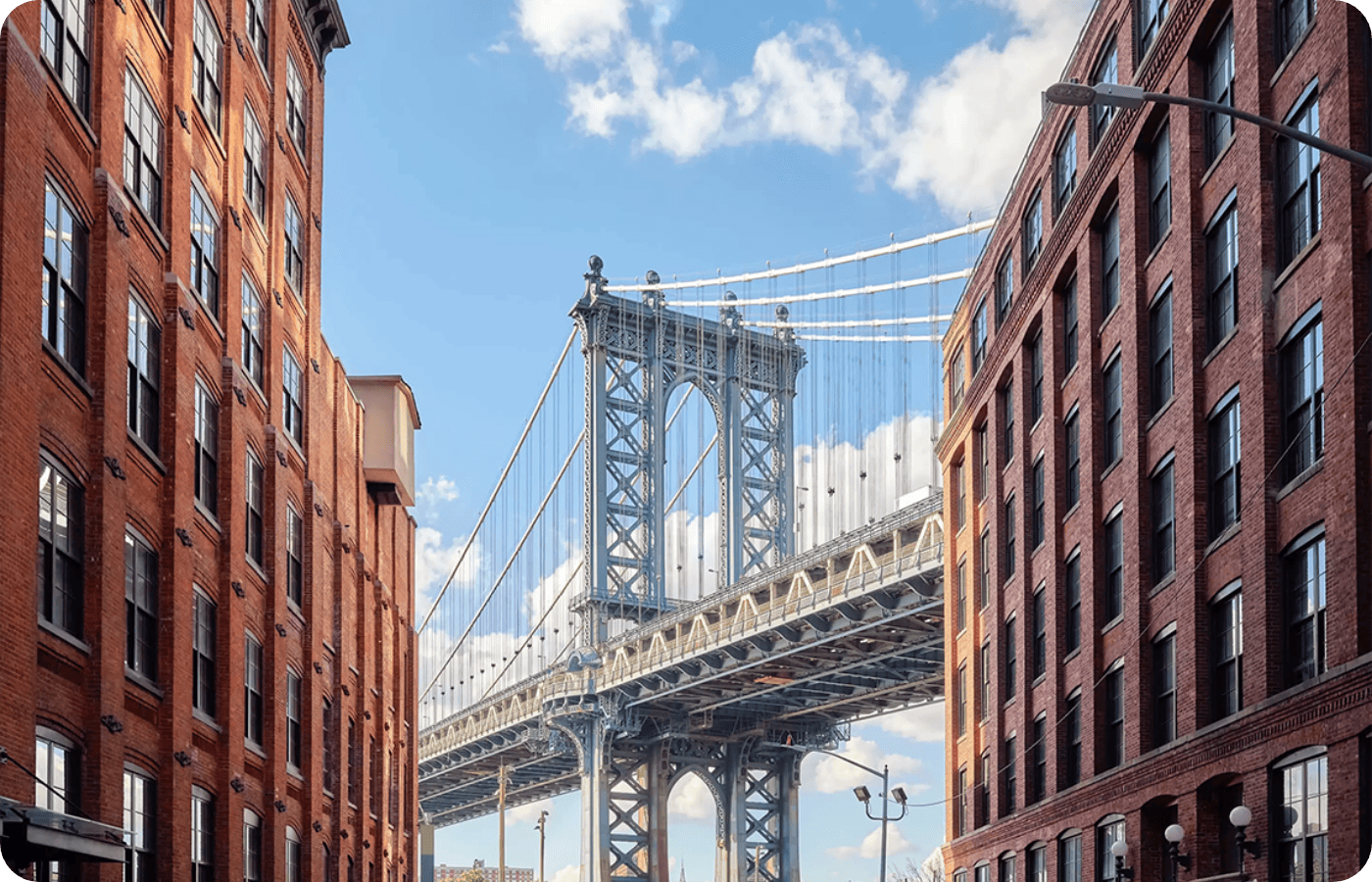 View of the Manhattan Bridge framed between two brick buildings under a blue sky with clouds.